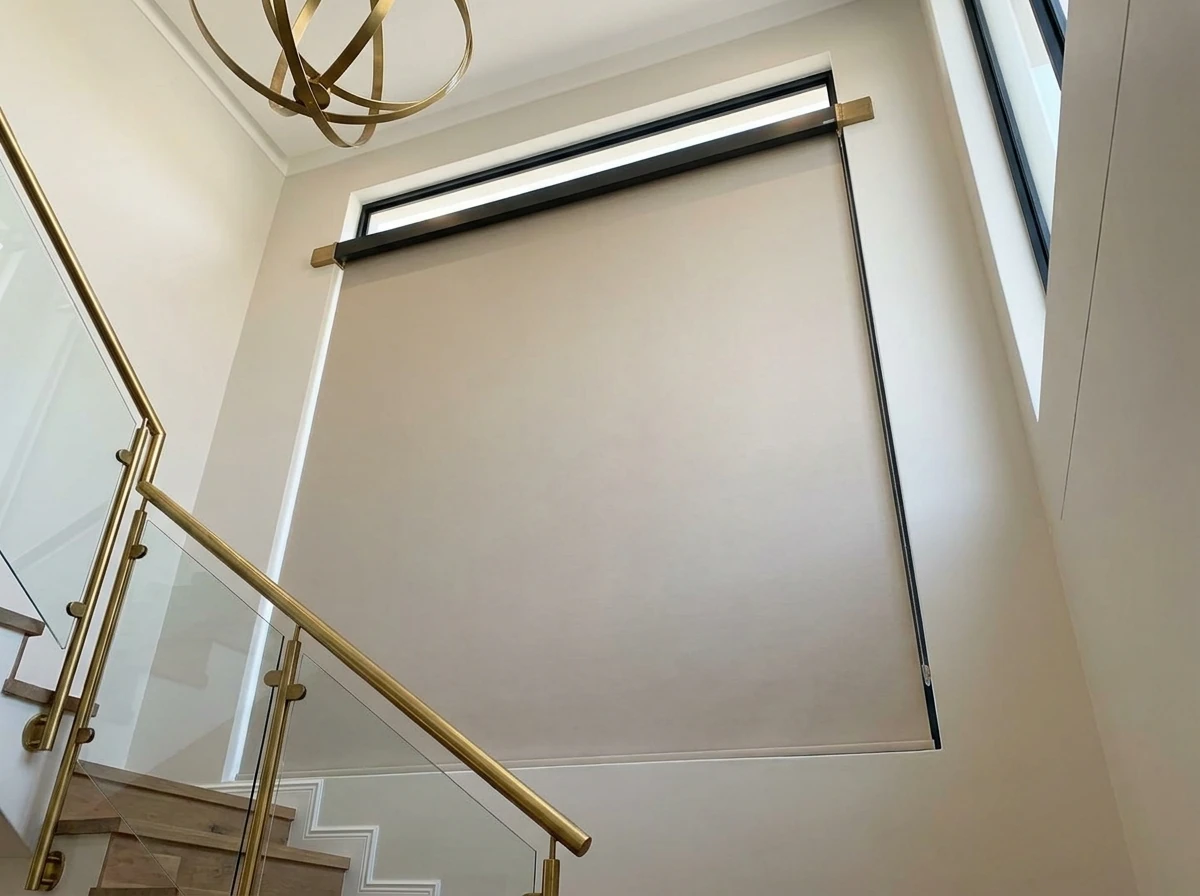 Motorised roller blind on an automated headrail above a double-volume stairwell window in a Bellville home